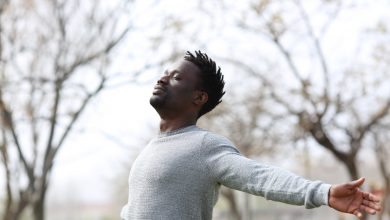 Black man breathing fresh air outdoors. Arms spread wearing a gray long sleeved shirt.