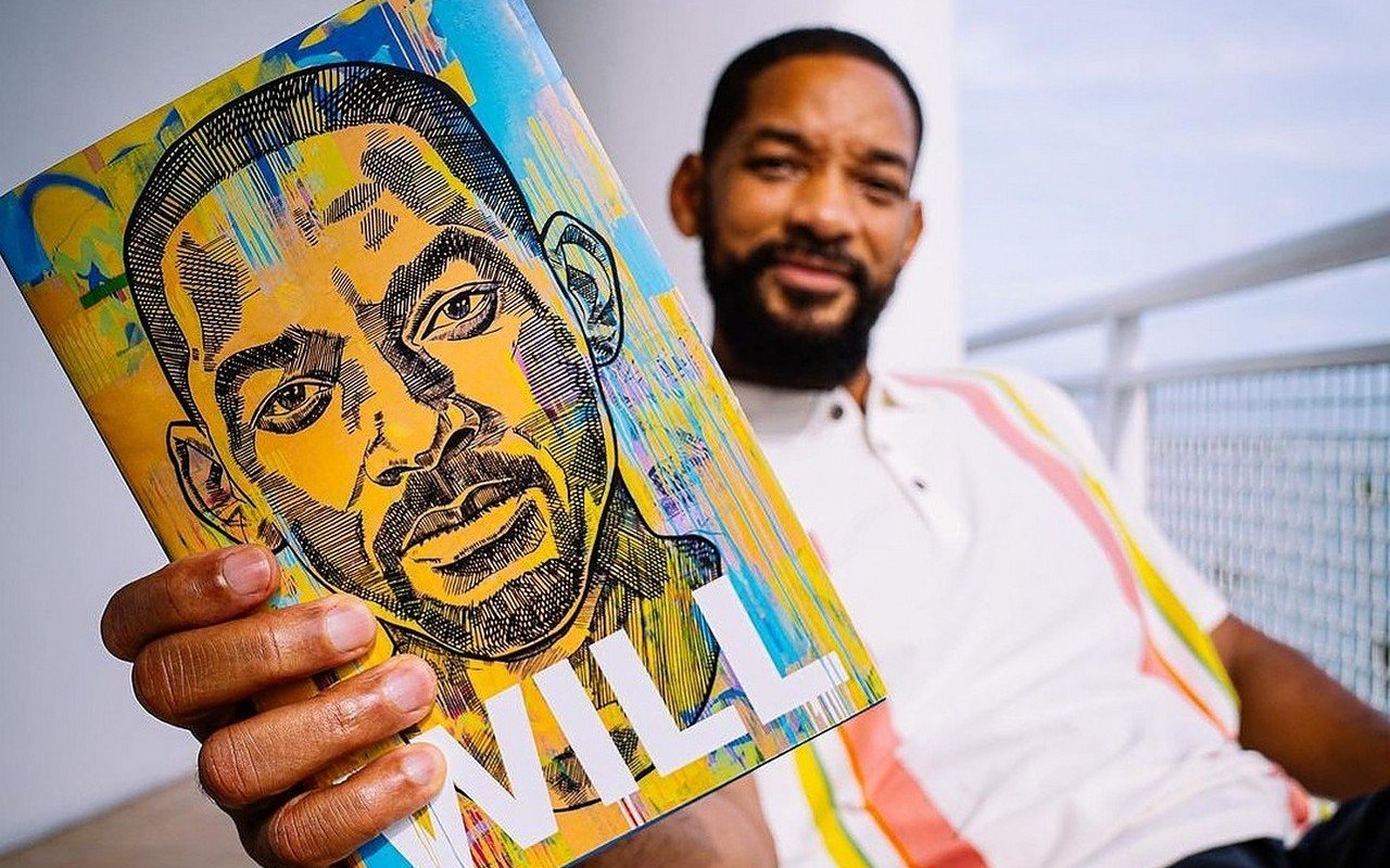 Will Smith holding his memoir, Will, towards the camera.