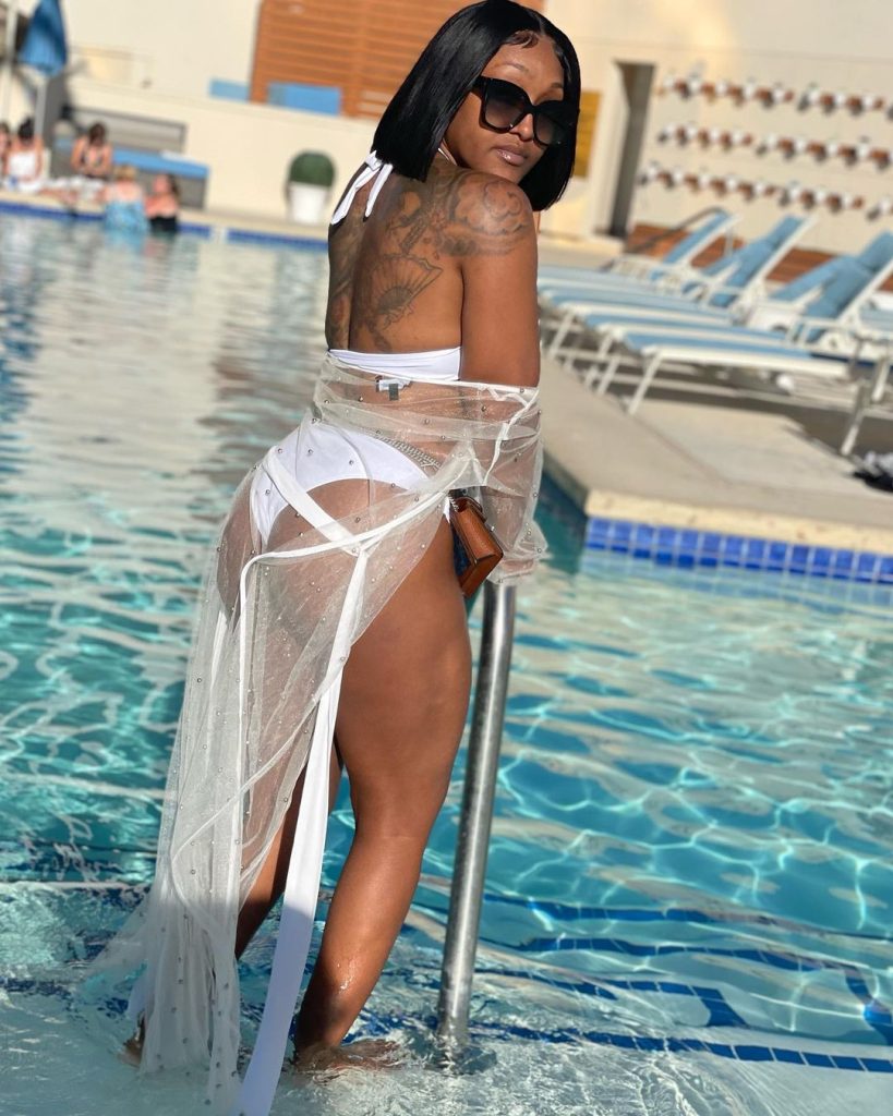 Shanquella Robinson standing at the edge of a pool wearing a white swimsuit.